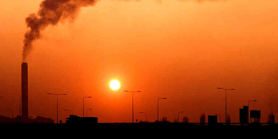 Smoke rising from smokestack against hazy sunny sky